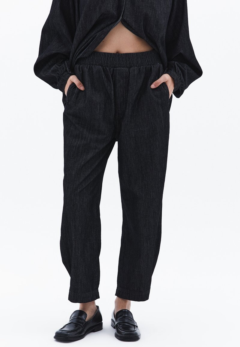 Svarta denimbyxor med avslappnad passform, elastisk midja, sidofickor och ett subtilt vertikalt randmönster. Matchas med svarta loafers.