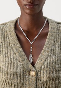 Colier din mărgele cu pandantiv în formă de pan�ă din argint, având mărgele albe și un cardigan texturat de culoare maro cu un nasture mare și design în V.