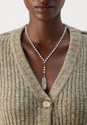 Perlekjede med sølv fjærvedheng, med hvite perler og en teksturert brun cardigan med stor knapp og V-hals design.