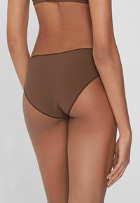 Bikinová spodní část s vysokým pasem v jednobarevné hnědé tkanině, s hladkou strukturou, bezešvým designem a kontrastním prošíváním na okrajích.