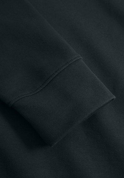 Poignet de sweat-shirt noir présentant une texture lisse et des coutures soignées, avec une coupe décontractée et un bord légèrement côtelé.