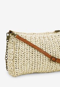 Borsa intrecciata color crema con una finitura texture, dotata di una tracolla in pelle marrone e un accento in catena color oro. Chiusura con zip nella parte superiore.
