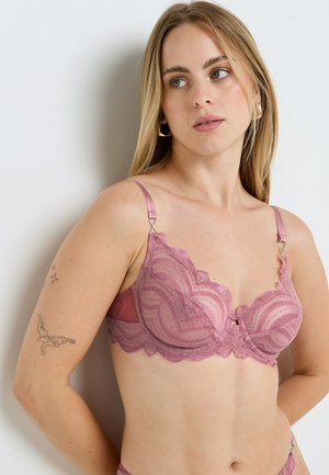 Soutien-gorge en dentelle de couleur rose pâle avec bords festonnés, motifs détaillés, armatures pour un bon maintien et bretelles réglables, orné d'un petit nœud central.