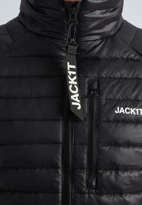 Veste matelassée noire avec col montant, dotée d'une fermeture éclair frontale, d'une poche poitrine et d'un détail logo. Texture lisse et brillante avec des coutures horizontales.