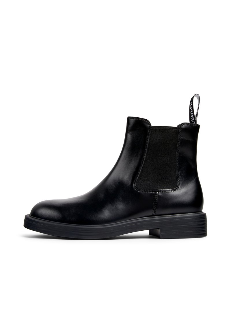 Black leather Chelsea ankle boot with elastic side panel, low heel, and pull tab with white text on a white background.