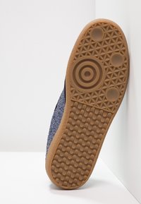 Semelle inférieure de basket bleue avec une semelle extérieure en gomme texturée, motifs circulaires et hexagonaux, et une finition supérieure pailletée.