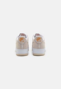 Beige suede sneakers met een witte rubberen zool, oranje Nike Air-logo op de hiel en een gevoerde kraag voor comfort. Minimalistisch ontwerp met een gestructureerde afwerking.