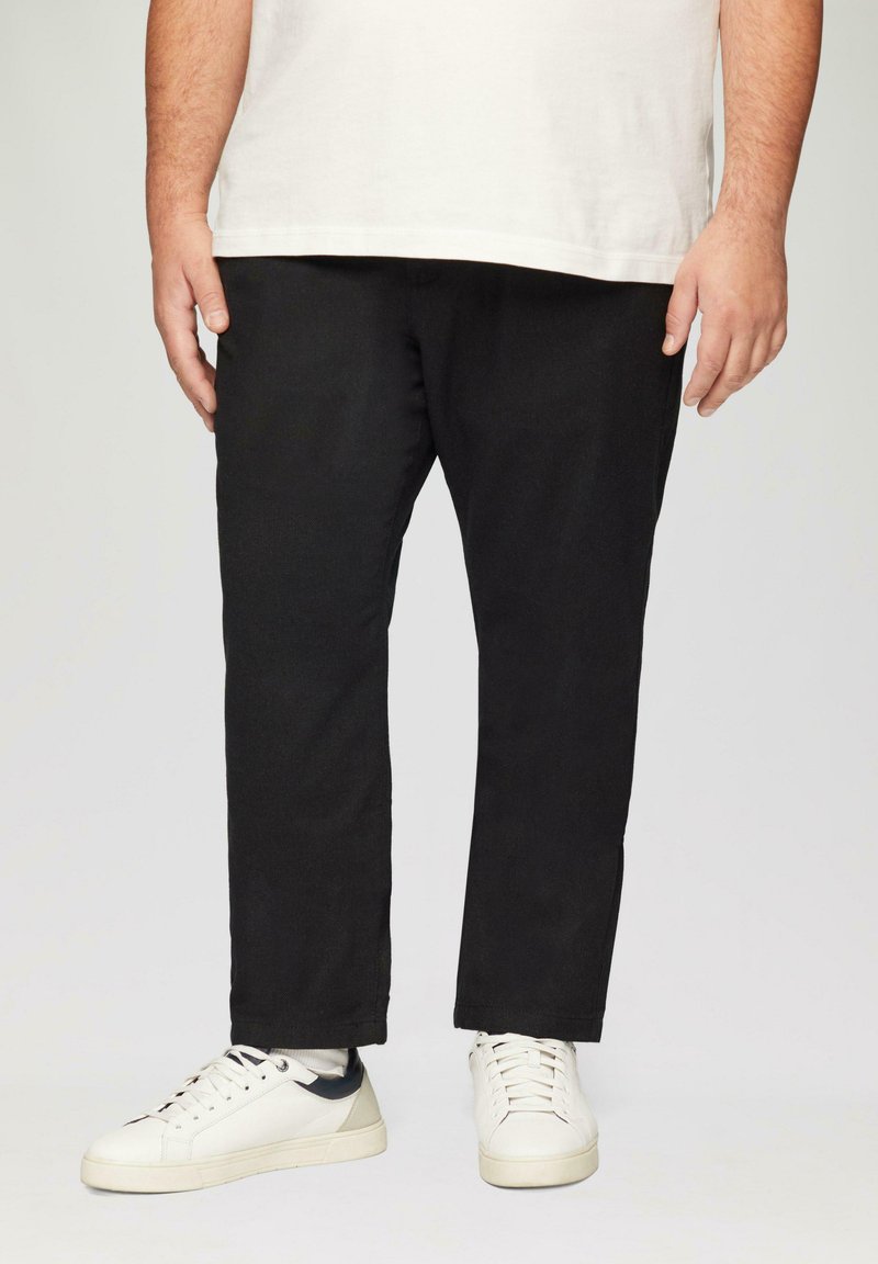 Pantalons en coton noirs avec une coupe droite et une longueur jusqu'à la cheville, associés à des baskets blanches avec un accent sombre sur le talon.