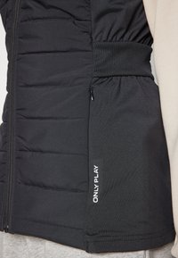 Čierna vypchávkovaná vesta s priliehavým strihom, elastickým pásom, zipsovou vreckom a bielym textom "ONLY PLAY" po boku.
