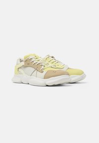 Footwear featuring a mix of pale yellow and beige synthetic materials, with a cushioned white sole, flat laces, and perforated accents.
