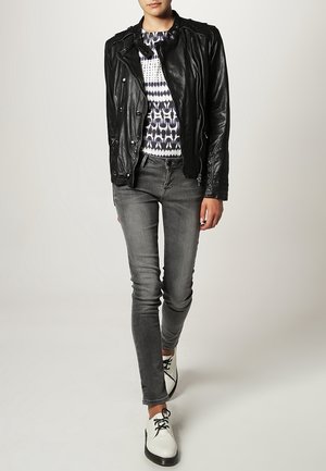 Giubbotto da moto in pelle nera, maglione stampato, jeans skinny grigi e scarpe bianche con dettagli neri. Texture liscia e design aderente.