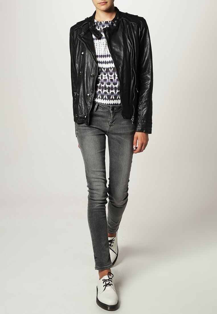 Svart läderbikerjacka, mönstrad tröja, grå skinny jeans och vita skor med svarta accenter. Slät textur och figursydd design.