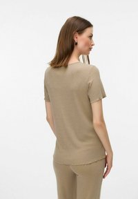 Top beige de manga corta fabricado en tejido acanalado, con un escote redondo y un corte relajado, con sutiles bordes deshilachados en las mangas y el dobladillo.