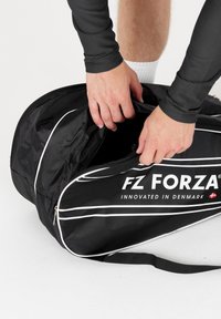Musta urheilukassi, jossa on valkoisia yksityiskohtia, valmistettu kestävästä kankaasta. Varustettu vetoketjullisella avauksella ja logolla "FZ FORZA", joka on näkyvästi esillä.