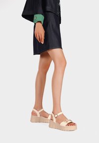 Sandali platform beige con cinturini alla caviglia regolabili e dettaglio della fibbia lucida. Suola testurizzata e materiale superiore liscio.