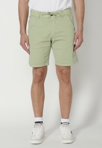 Pantalones cortos verdes claros con una cintura elástica y cordón, que cuentan con bolsillos laterales y un diseño de pierna recta. Llevados con zapatillas blancas.