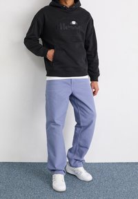 Felpa nera con cappuccio e logo, tasca frontale, abbinata a pantaloni azzurri e sneakers bianche. Tessuto liscio e vestibilità comoda.