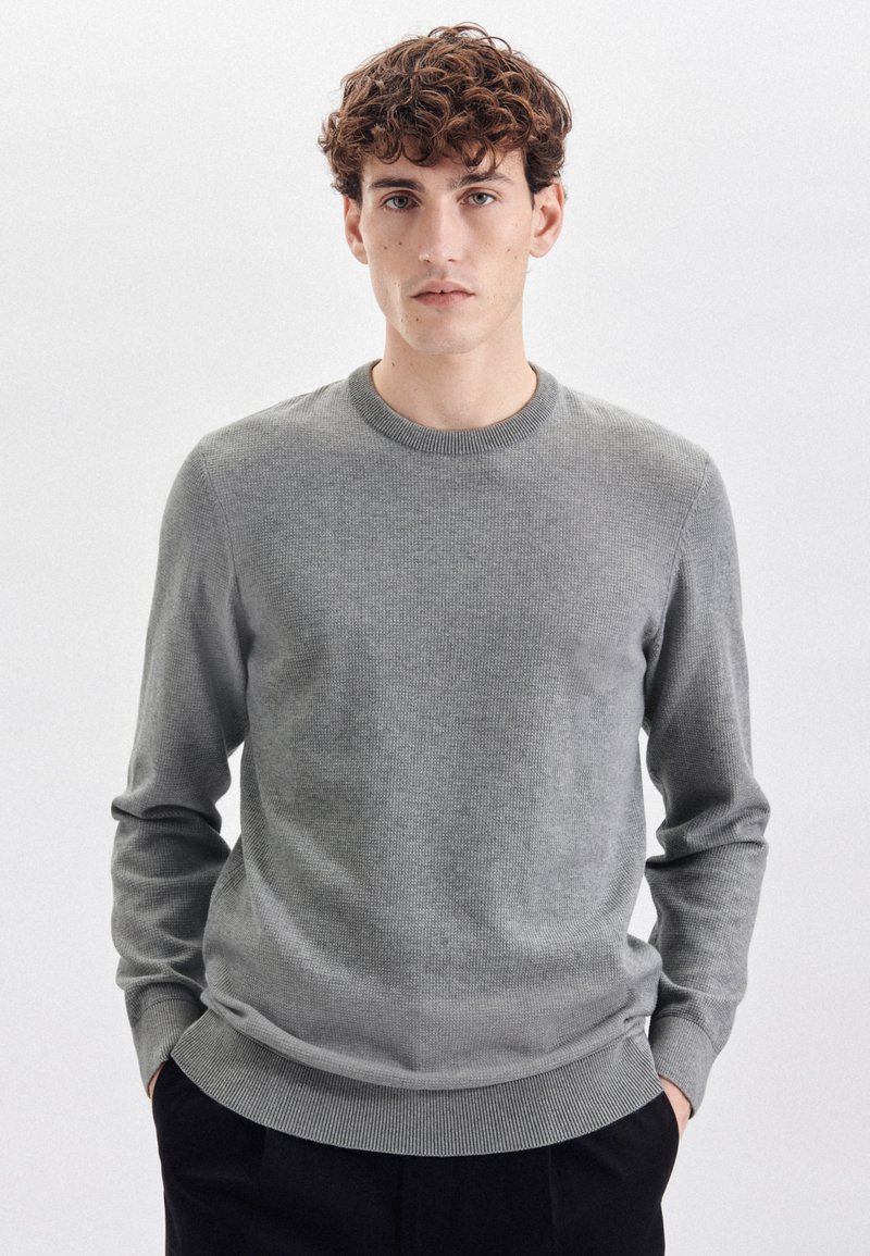 Maglione grigio lavorato a maglia con scollatura rotonda, polsini e orlo a coste. Il tessuto ha una trama sottile e una silhouette aderente.