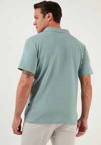 Lichtblauwe polo met een gestructureerde afwerking, korte mouwen en een klassieke kraag, getoond op een model van achteren bekeken.