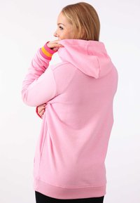 Rosa hoodie med huva och långa ärmar, med randiga detaljer i gult och orange vid mudden, tillverkad av mjukt material.