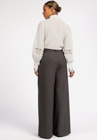 Lichtgrijze blouse met textuur en kantdetails op de mouwen, gecombineerd met donkergrijze pantalon met krijtstrepen en wijde pijpen. Achteraanzicht, met een ontspannen pasvorm.