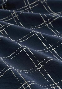 Tissu marine avec des lignes blanches en pointillé formant un motif de grille, affichant une texture lisse et un tombé doux. Idéal pour le rembourrage ou les textiles.