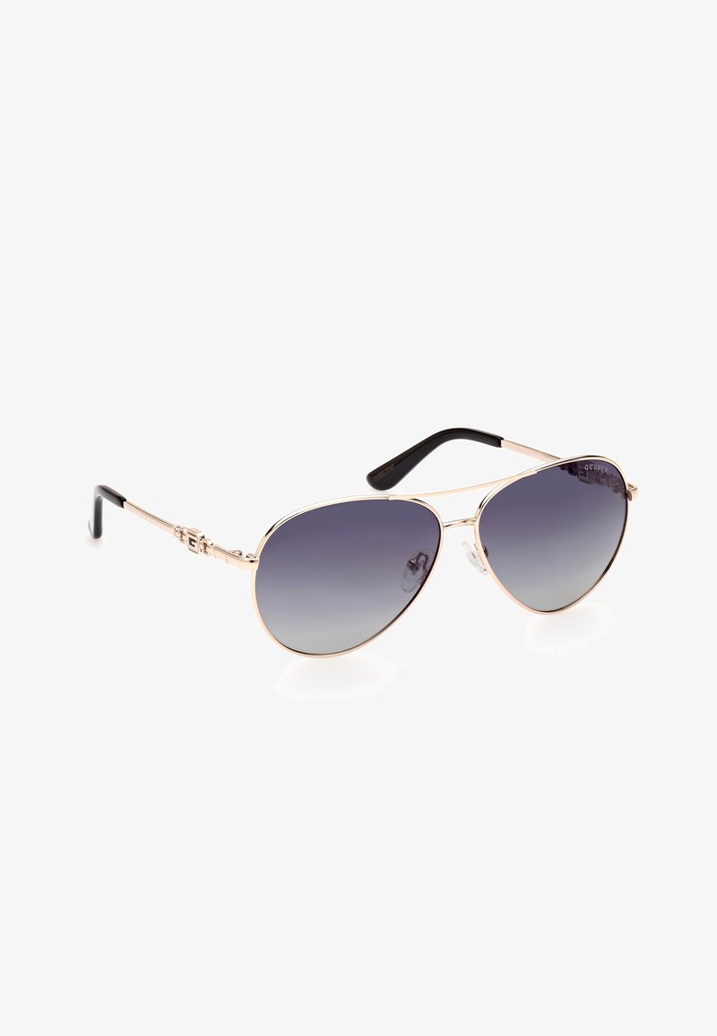 Des lunettes de soleil aviateur avec des verres gris dégradés, une monture en métal doré et des embouts de branches en plastique noir texturé. Présente des détails de logo sur les côtés.