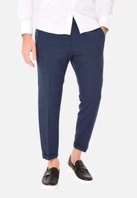 Pantaloni blu navy a gamba affusolata realizzati in un tessuto morbido, con polsini arrotolati e abbinati a scarpe slip-on nere per un look casual.