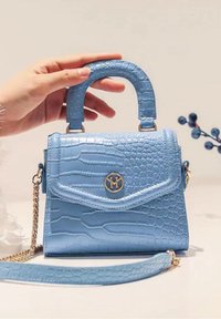 Blå handväska med krokodilprägling, med ett handtag upptill och avtagbar kedjerem. Har en fälllockstängning och en guldfärgad logotypdetalj på framsidan.