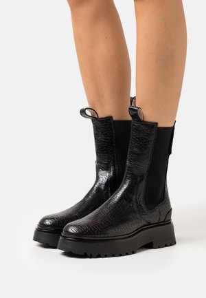 Botines negros de cuero texturizado con acabado brillante. Cuentan con paneles laterales elásticos y tiradores para facilitar su colocación. Suela de goma chunky.
