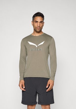 Olijfgroene langemouwen t-shirt met een wit logo en v-vormige accenten, gecombineerd met zwarte shorts met een textuurafwerking en ritszakken.