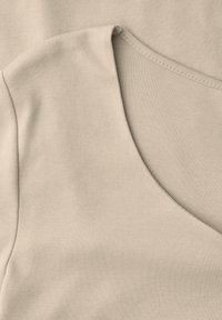 Tissu en coton beige avec un gros plan sur un décolleté en V et une couture d'épaule présentant des détails de piqûre soignés.