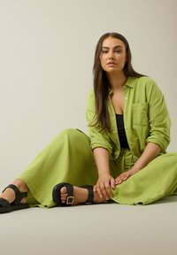 Limoengroene linnen shirt en bijpassende broek, met een relaxte pasvorm, gecombineerd met zwarte sandalen met een vierkante gesp.