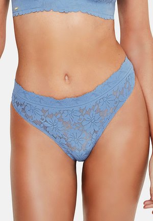 Vrouwelijke torso met een lichtblauwe bloemenkant beha en bijpassende hoog uitgesneden kanten slip op een witte achtergrond.