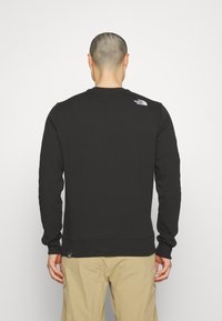 Sudadera negra de manga larga y cuello redondo. Presenta un pequeño logotipo blanco en la parte superior de la espalda. Exhibida sobre un fondo blanco liso.