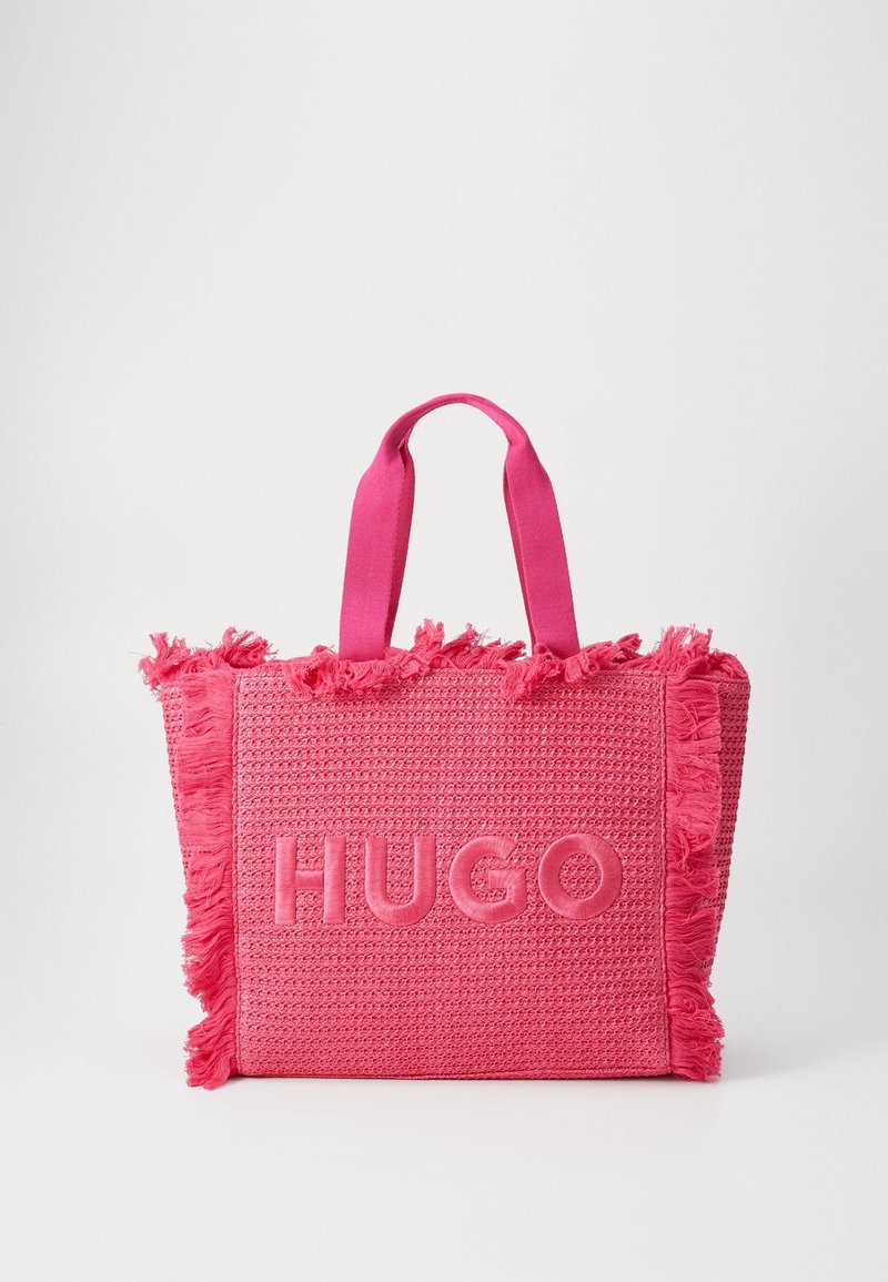 Růžová taška přes rameno s třásněmi, na jedné straně s vyraženým logem "HUGO" a pevnými látkovými rukojeťmi pro nošení.