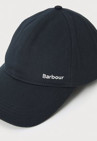 Sötétkék sapka ívelt csúccsal, texturált anyagból készült. Elöl fehér hímzett "Barbour" logó található.