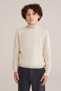 Svijetlosmeđi turtleneck pulover izrađen od mekanog materijala, s rebrastim ovratnikom i manžetama, uparen s tamnim korden trapericama.