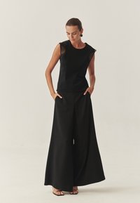 Fekete, ujjatlan felső átlátszó csipkével díszítve, széles lábú fekete nadrággal párosítva. Simább textúra, minimalista design, egyszerű sziluett.