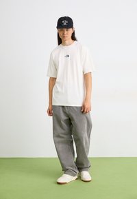 Biele tričko s krátkym rukávom s logom North Face, skombinované so sivými kordovými nohavicami a bielymi teniskami; čierna čapica s grafickým potlačou.