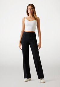 Black wide-leg trousers with a tailored fit, featuring a smooth texture and center crease. Paired with a white cropped tank top and white sneakers.
