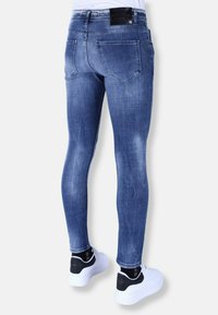 Skinny jeans in medium blue denim, met een vervaagde textuur, vijf zakken en een zwartleren label op de tailleband; gedragen met witte sneakers.