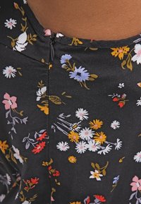 Gros plan sur un tissu noir avec un motif floral coloré et une fermeture éclair noire le long d'une couture près d'une peau mate.