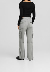 Pantaloni cargo grigi con una vestibilità rilassata, tasche laterali e dettagli a toppa, abbinati a un top aderente nero a coste off-the-shoulder.