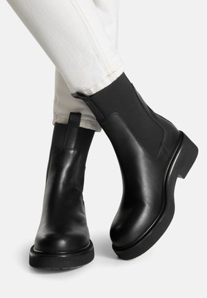 Schwarze Chelsea-Stiefel aus Leder mit elastischen Seitenpaneelen, abgerundeter Spitze und niedrigem, gestapeltem Absatz. Glatte Textur und strapazierfähige Gummisohle.