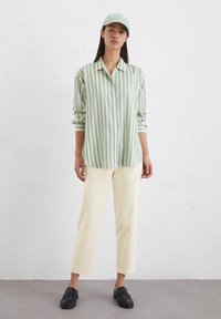 Lysegrønn og hvitstripet bluse med krage, sammen med kremfargede, kortbukser og svarte loafers, båret med en matchende caps.