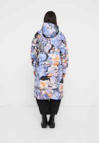 Manteau matelassé long à fleurs avec un mélange de nuances bleues, orange et violettes. Doté d'une capuche, de poignets élastiques et d'une coupe mi-mollet.