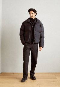 Veste matelassée noire avec un col haut, assortie à un pantalon cargo noir. Chaussures noires chunky. Texture lisse, design contemporain.