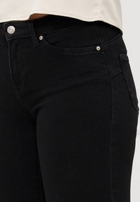 Svarta denimjeans med en figurnära passform, med silverfärgade detaljer på fram- och bakfickorna, samt en slät yta.
