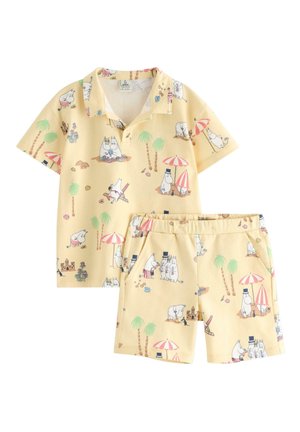 Completo per bambini composto da camicia gialla a maniche corte e pantaloncini con personaggi di ippopotami dei cartoni animati, palme, ombrelloni e scene di castelli di sabbia sulla spiaggia.